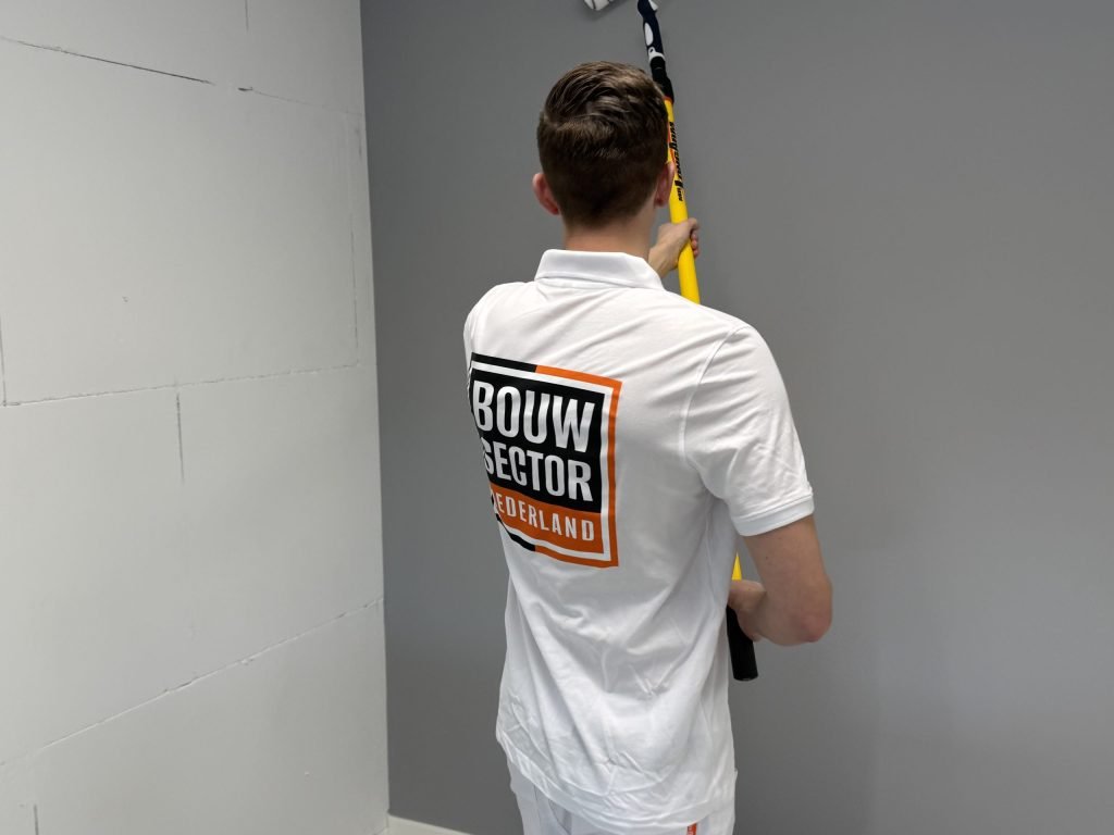 Schilder met het Bouwsector-logo op zijn rug rolt een grijze wand naast een muur van kale blokken