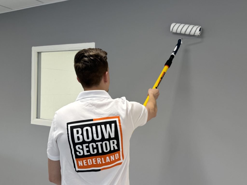 Achteraanzicht van een schilder die een grijsblauwe wand rolt naast een raam met witte omlijsting
