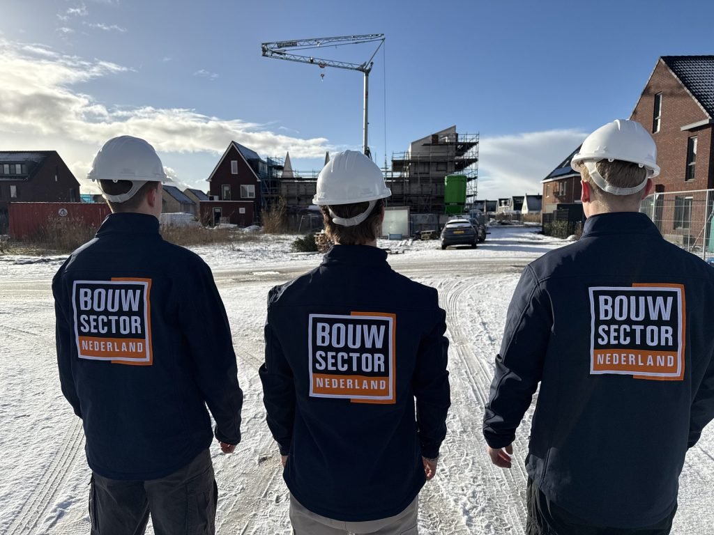 Drie mensen van Bouwsector Nederland met witte bouwhelm kijken naar een nieuwbouwstraat in de sneeuw