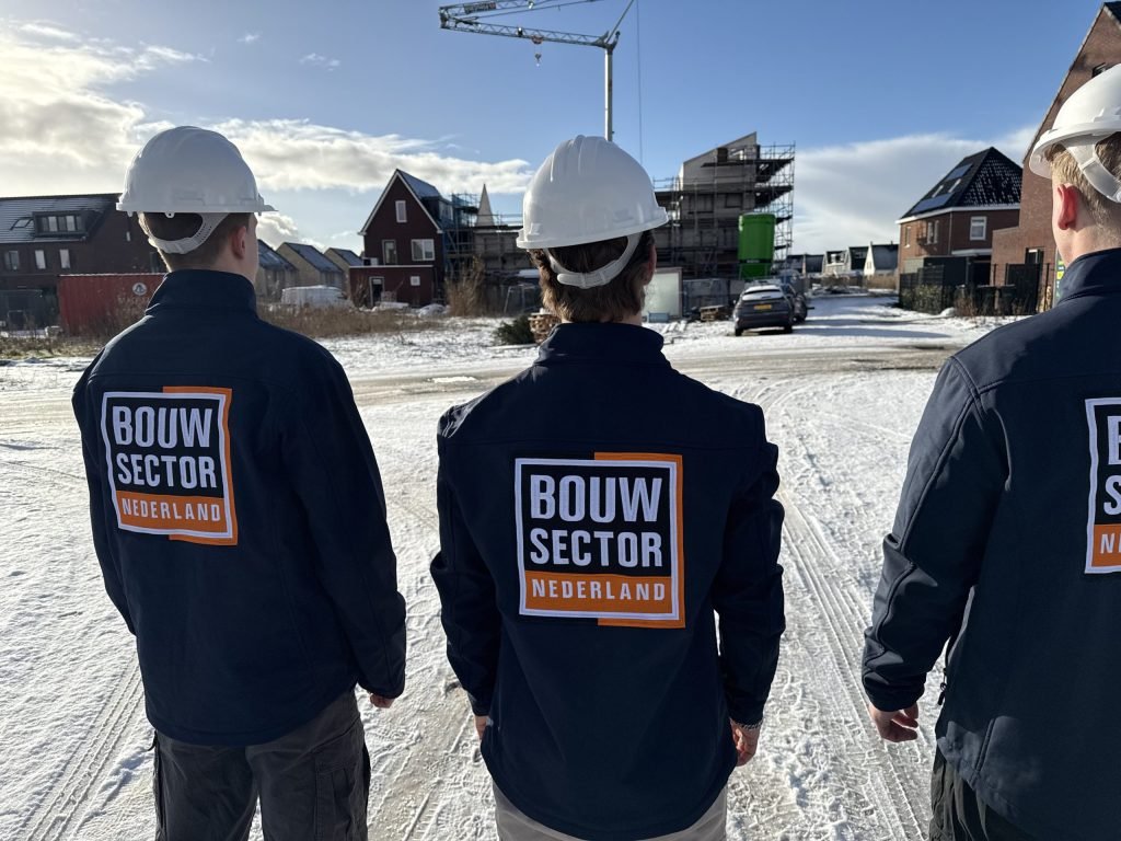Drie vakmensen van Bouwsector Nederland met witte helm kijken naar nieuwbouwwoningen en een bouwkraan